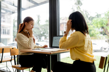 Fototapeta premium Young businesswomen collaborating on project, analyzing data on laptop in modern coworking cafe