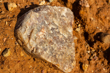 Raw white vein quartz boulder with a rough natural cleavage surface lying on red earthy quarry soil, close-up texture shot of a crystalline mineral specimen in mining environment © PhotoChur