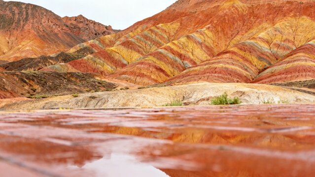 Colorful layered rock formations reflected in a shallow water pool in a desert landscape