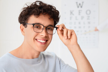Vision care and eye health, young man wearing new prescription glasses during an optometry checkup with a vision chart in the background © Pixel-Shot