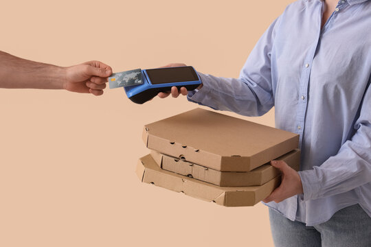 Contactless payment for food delivery, customer paying with credit card for pizza boxes held by courier in a secure transaction on beige background