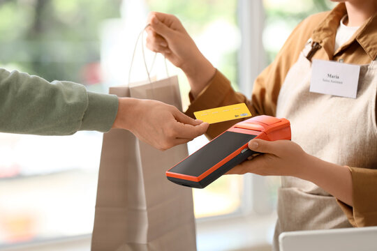 Contactless payment and retail shopping, customer paying with credit card at store checkout counter with sales assistant holding a payment terminal