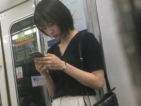 電車内でスマートフォンを見る黒いブラウス姿の成人女性