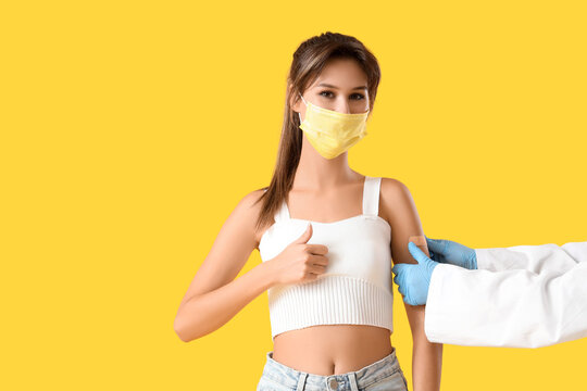 Doctors hands applying patch on woman in medical mask showing thumb-up after vaccination against yellow background. Immunity concept