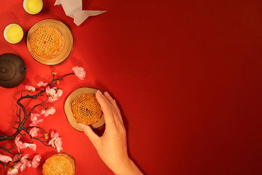 Flat lay of hand holding mooncake on red background for Mid-Autumn Festival with copy space