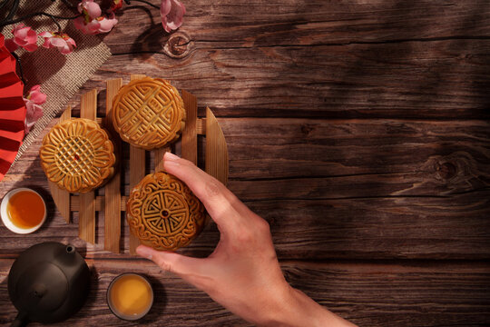 Hand holding mooncake on wooden table for Mid-Autumn Festival tea pairing