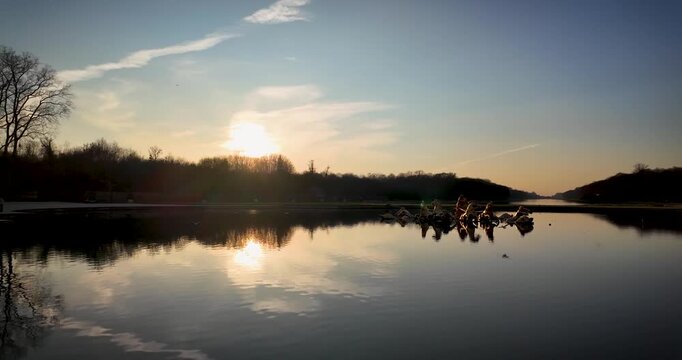Sunset view of Apollo Fountain in the Gardens of Versailles, with the gilded chariot sculpture, calm water reflections and Grand Canal creating a dramatic historic landscape.