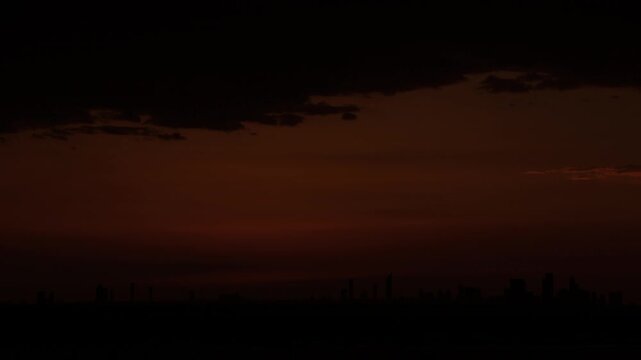 The sun sets behind the silhouetted Abu Dhabi skyline in an orange sky, viewed from Yas Island, Time Lapse