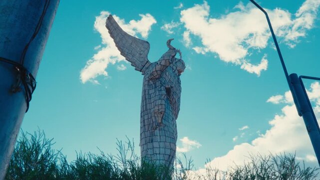 Low-angle view of the Virgin of El Panecillo statue in Quito, Ecuador, against a bright blue sky with scattered clouds
