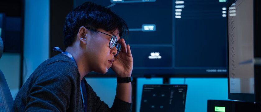 Asian Cybersecurity Analyst Concentrating on Network Data Across Multiple Computer Screens During a Late-Night Shift