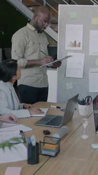 African American businessman making report speaking to group of colleagues at business meeting in office. Teamwork and professional cooperation concept.