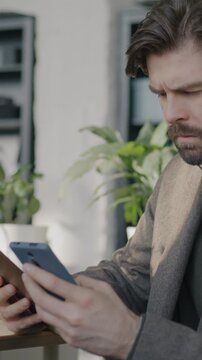 Businessman reading document and using smartphone concentrated on corporate online communication in office. Modern gadget and business concept.