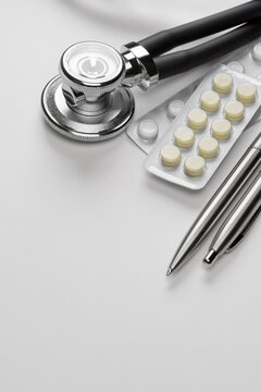 Stethoscope, pills, and pens on white surface