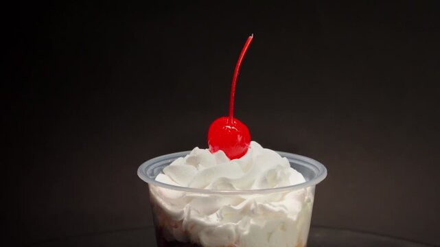 Creamy dessert with maraschino cherry in plastic cup spinning on black background.
