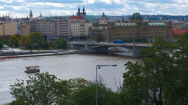 Vltava river flowing through prague with traffic on the bridge. Traffic flows on the bridge over vltava river in prague, with boats navigating the waterway and the cityscape in the background