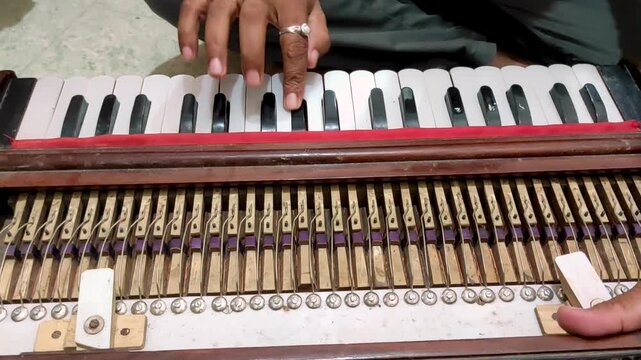 Close-up video footage of a vintage traditional harmonium being played, showing its keyboard, exposed metal reeds, wooden construction, mechanical components, and the musician's hands.