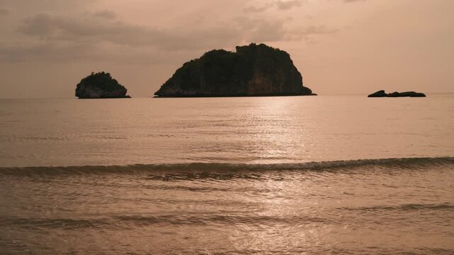 Golden hour tropical sea landscape with soft waves and islands silhouette.