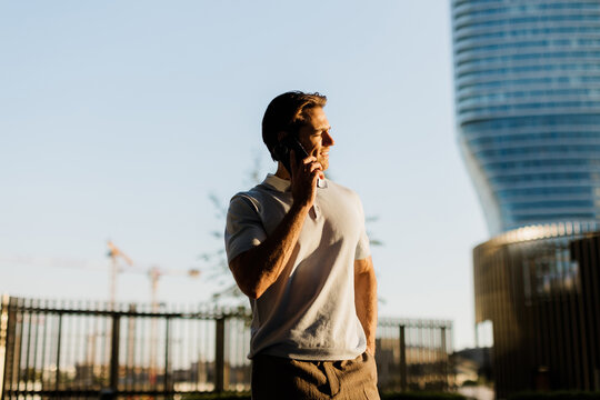 Man talking on the phone with a modern building in the background during sunset