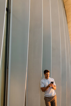 Relaxed moment of a young man using his phone by a sleek architectural wall