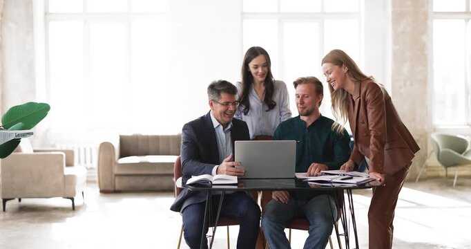 Office coworkers group engaged in teamwork on laptop and paperwork discussing project ideas reviewing digital presentation analyzing online information preparing electronic document together at table