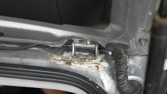 Rusty metal hinge on a silver car trunk lid frame.