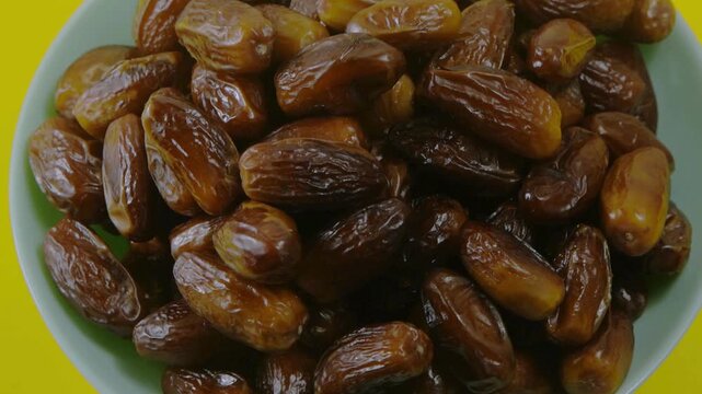 Dried date fruit in a bowl, organic sweet dates on yellow background, healthy mediterranean snack and ramadan food