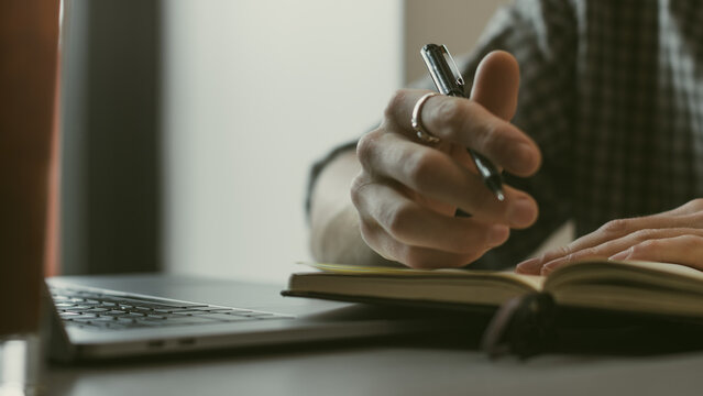 Hand Writing in Journal Next to Laptop and Glasses