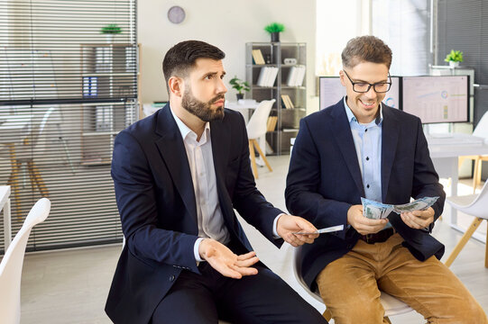 Coworkers men compare wages in office payroll inequality. One man counts a paycheck another stacks bonus cash, showing salary disparity among employees. Comparison of workplace pay inequality.