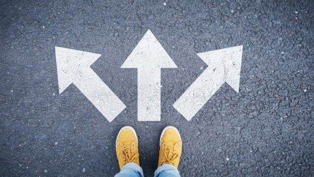 Person in yellow sneakers stands before three arrows painted on asphalt. This represents a decision making concept for business success and life choices.
