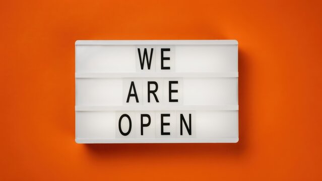 A cinema-style lightbox displays the message We Are Open against a bright orange background. Use for business reopening announcements and promotional signage.