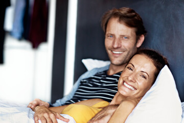 Obraz premium Portrait, couple and smile in bed together for rest, happiness and comfortable on weekend in home. Man, woman and relax with break, care and cozy in bedroom for bonding in relationship in apartment