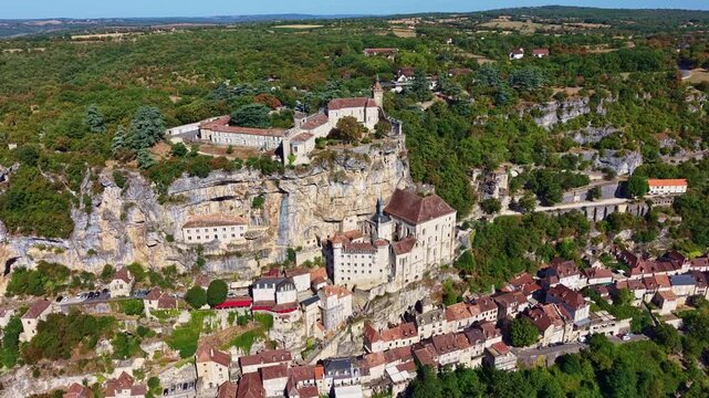 High aerial view approaches Rocamadour, revealing its tiered historic buildings before tilting down near the upper fortified town.