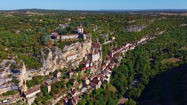 High drone view moves toward Rocamadour, revealing the historic town, cliffside buildings and upper fortifications across the steep valley.