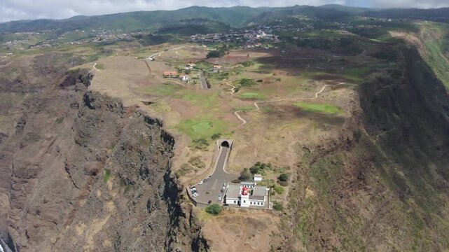 Remote and peaceful setting of the Ponta do Pargo golf course. Surrounded by cliffs and ocean, the course appears as a green oasis in a rugged volcanic landscape. Drone moving backwards.