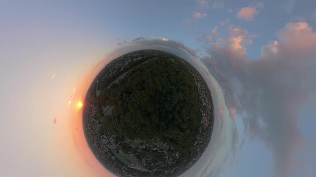 Cinematic aerial tiny planet view at sunset over a suburban landscape, winding parkway and woodland stretching toward the horizon, capturing tranquil evening light in the suburbs. The camera dolly in.