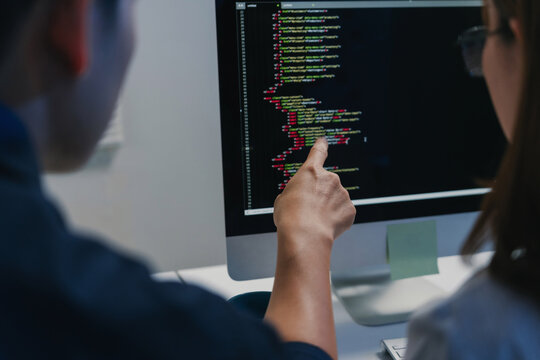 Developers collaborating on computer screen pointing at coding lines