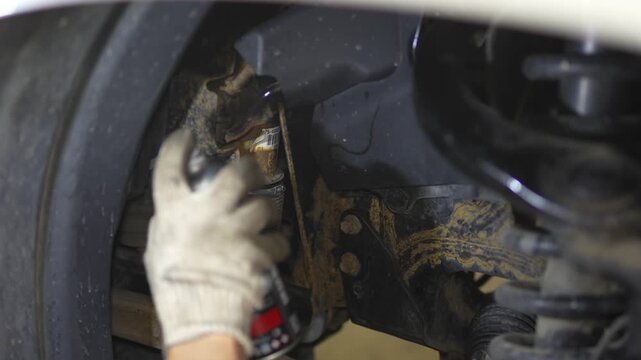 Man spraying black protective anti-corrosion coating onto car chassis part.