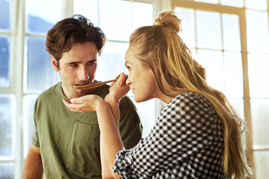 Couple, cooking and feed in kitchen with spoon, romantic partner and taste test for bonding together. People, dating and sample food in home for lunch preparation, relationship and help with recipe.