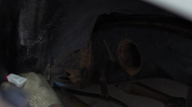 Man spraying black protective anti-corrosion coating onto car chassis part.