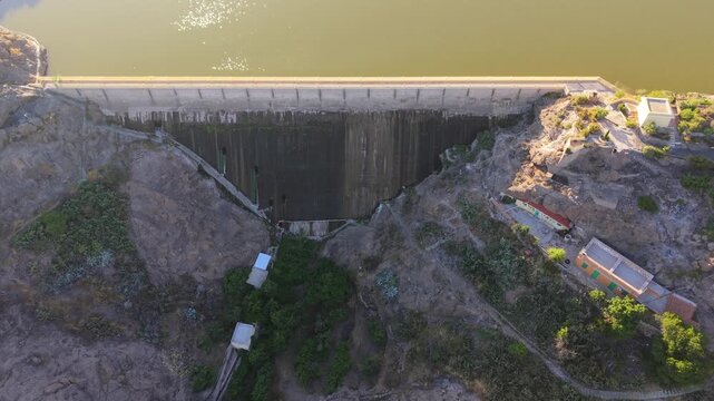 Cinematic drone shot flying over the impressive concrete structure of Las Ninas dam, revealing the deep, rocky canyon below at sunset