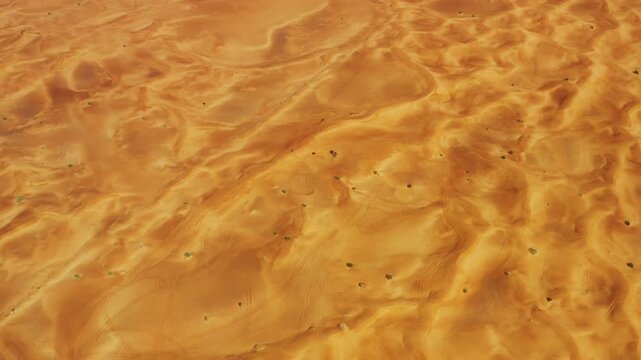 High aerial drone view moving slowly above Dubai desert dunes, revealing abstract natural curves, ridges and patterns in the sand.