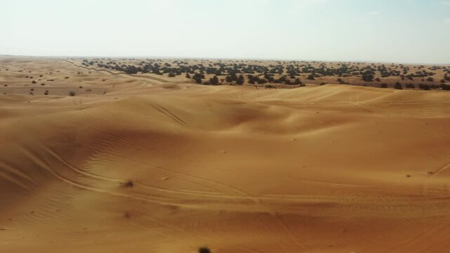 Drone tracks an off road buggy racing over golden dunes in the Dubai desert