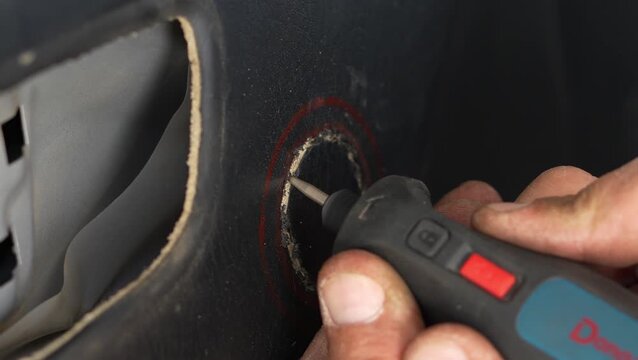 Man using a rotary tool to cut car door card.