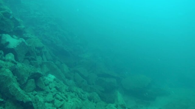 Underwater footage exploring an old flooded limestone quarry, revealing a rugged submerged landscape of broken rocks, stone debris and exposed quarry terrain.