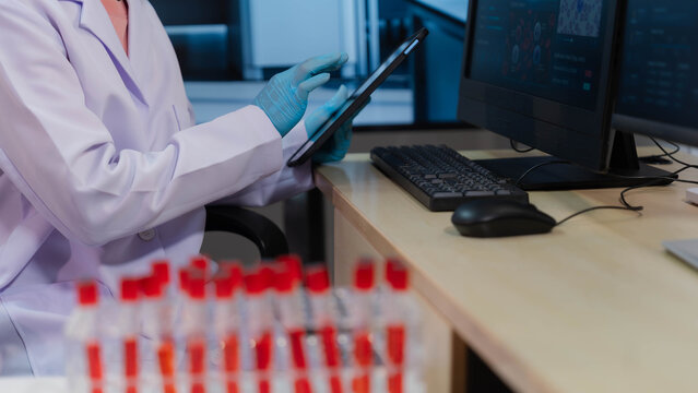 Scientist holding blood sample test tube and analyzing data on computer screen in laboratory