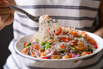 Thai spicy glass noodle salad with minced pork and shrimp (Yum Woon Sen) on a white plate holding by woman hand and eat © nungning20