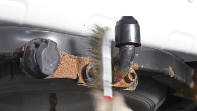 Man cleaning a rusty car tow hitch with wire brush.