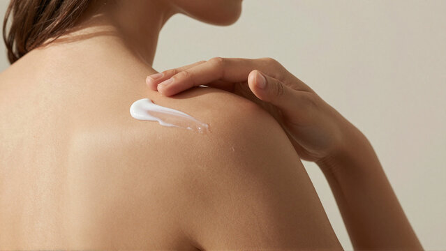 Woman applying moisturizing body cream to shoulder during summer skincare routine at home