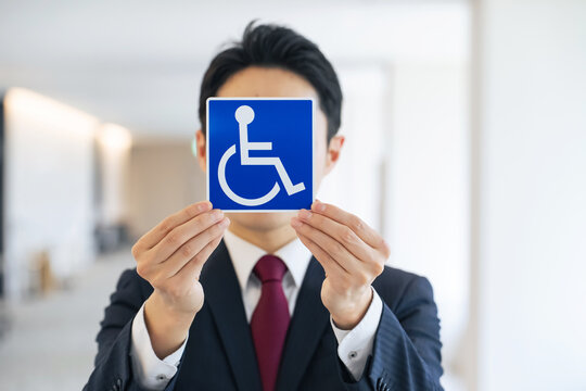 車いすマークを持つ男性。障害者、高齢者、バリアフリー、介護、福祉、安全、安心、思いやり、駐車場、施設