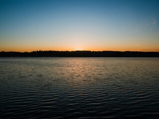 Serene sunset over calm lake with dark silhouette of distant forest © Nazar